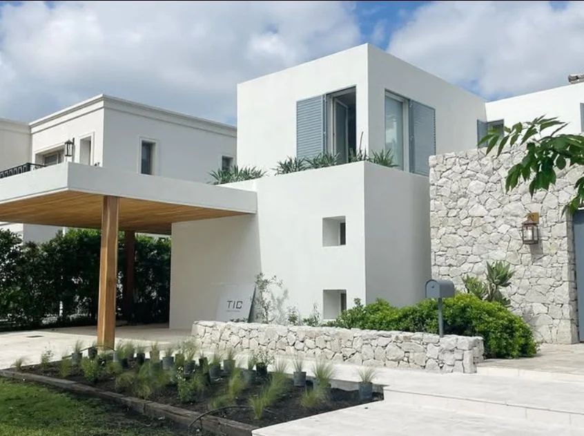 Fachada blanca con muro de piedra y galería de madera, proyecto de Estudio TIC